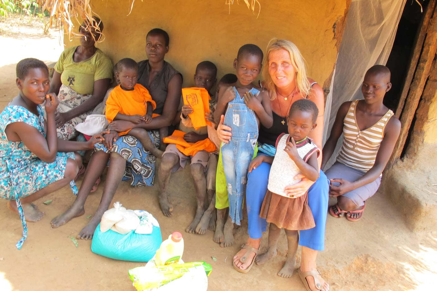 Gruppe vor Haus in Dorf in Afrika mit Grundnahrungsmitteln im Vordergrund