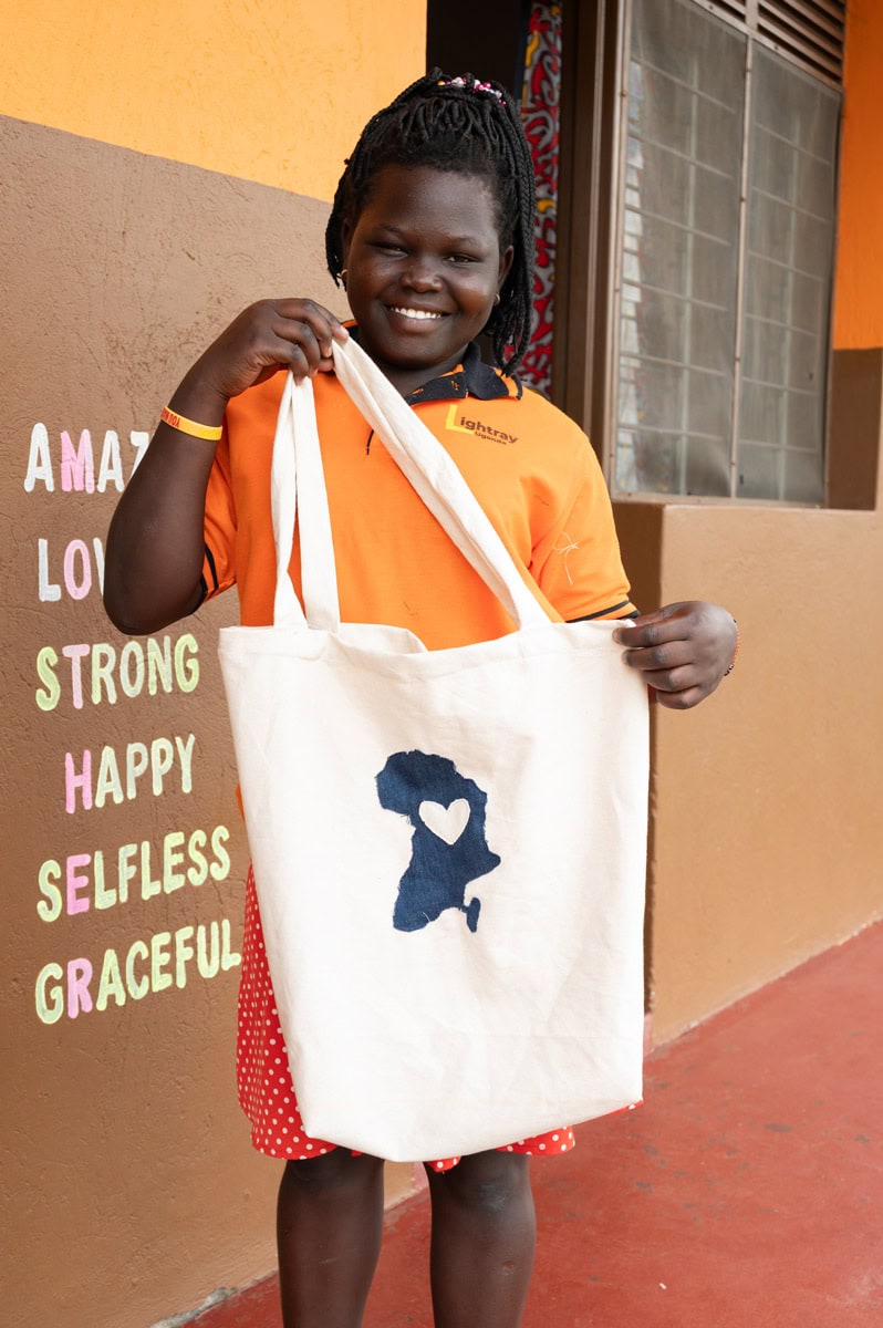 Ein Mädchen lächelt und hält eine Stofftasche mit einem aufgedruckten Herz und Afrikas Umriss.