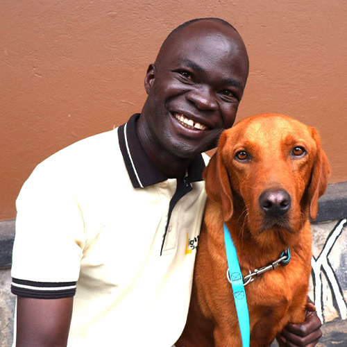 In this image, a person is joyfully smiling and embracing a brown dog with a blue leash.