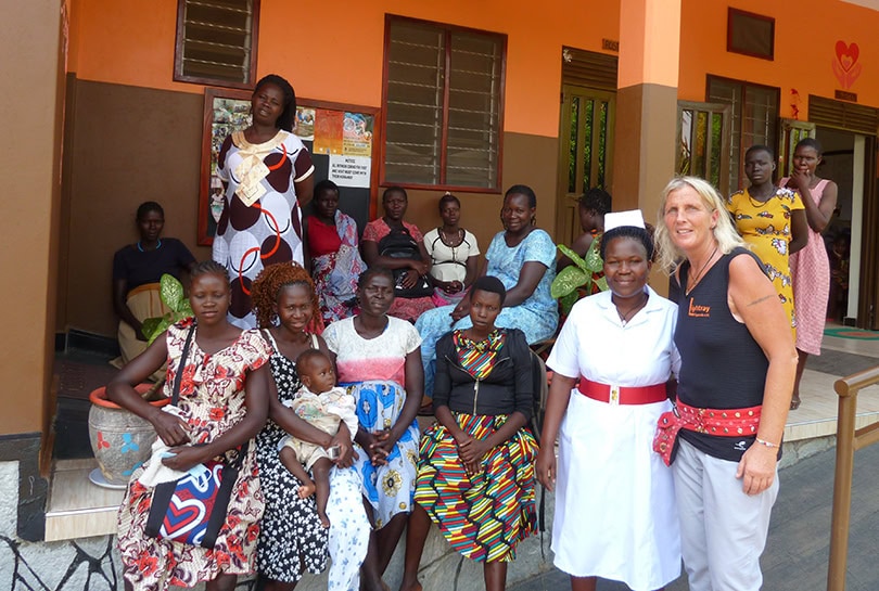 Eine Gruppe afrikanischer Frauen mit bunten Kleidern, lächelnd vor einem orangefarbenen Gebäude.